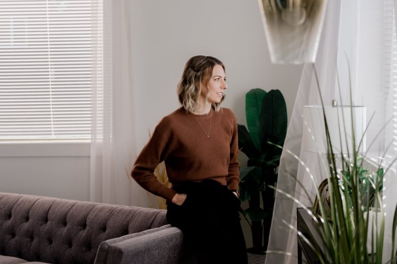 Woman sitting on the arm of a grey couch with plants around her