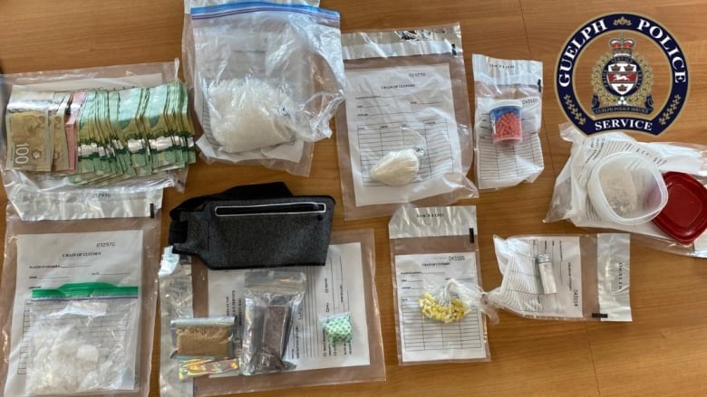 Nine ziploc bags containing illegal drugs are on a table for display beside a large wad of Canadian cash 