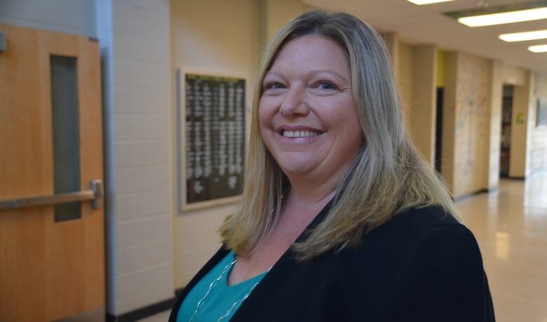 A smiling blonde-haired woman standing in a school hallway 