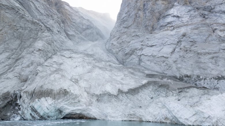 A glacier is seen above a body of water. After a landslide the mountaintop is now gone.