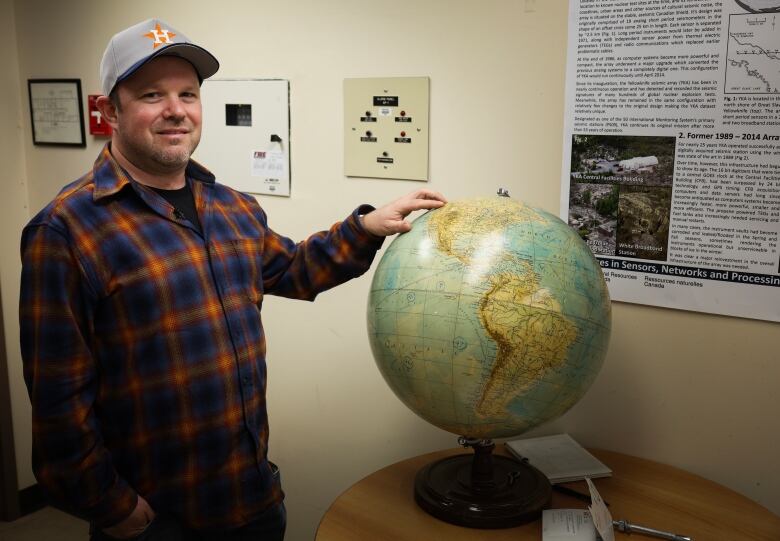 A man stand next to a globe with his hand on it 