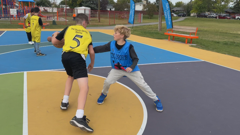 A male youth wearing a yellow jersey bounces a ball while another male youth wearing a blue jersey tries to stop him.