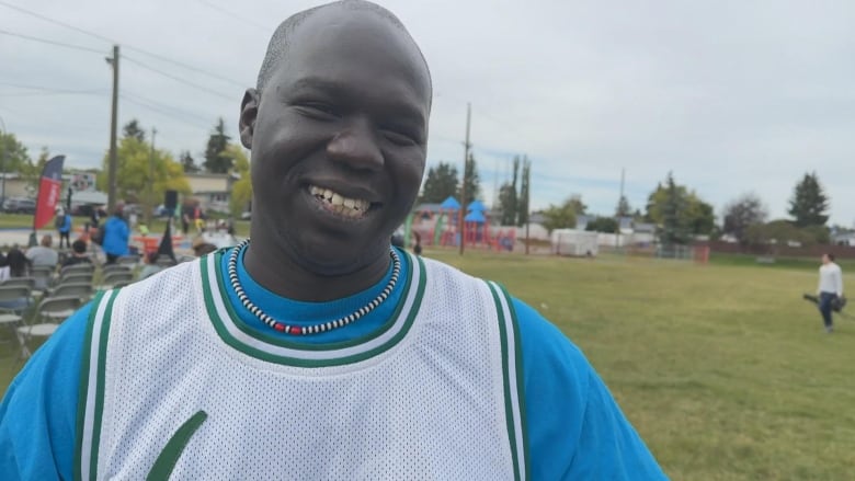 A black man wearing a bright blue tshirt smiles at the camera.