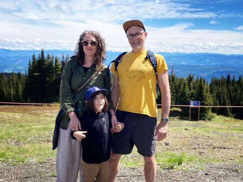 A husband and wife standing outside with their young son in front of them.