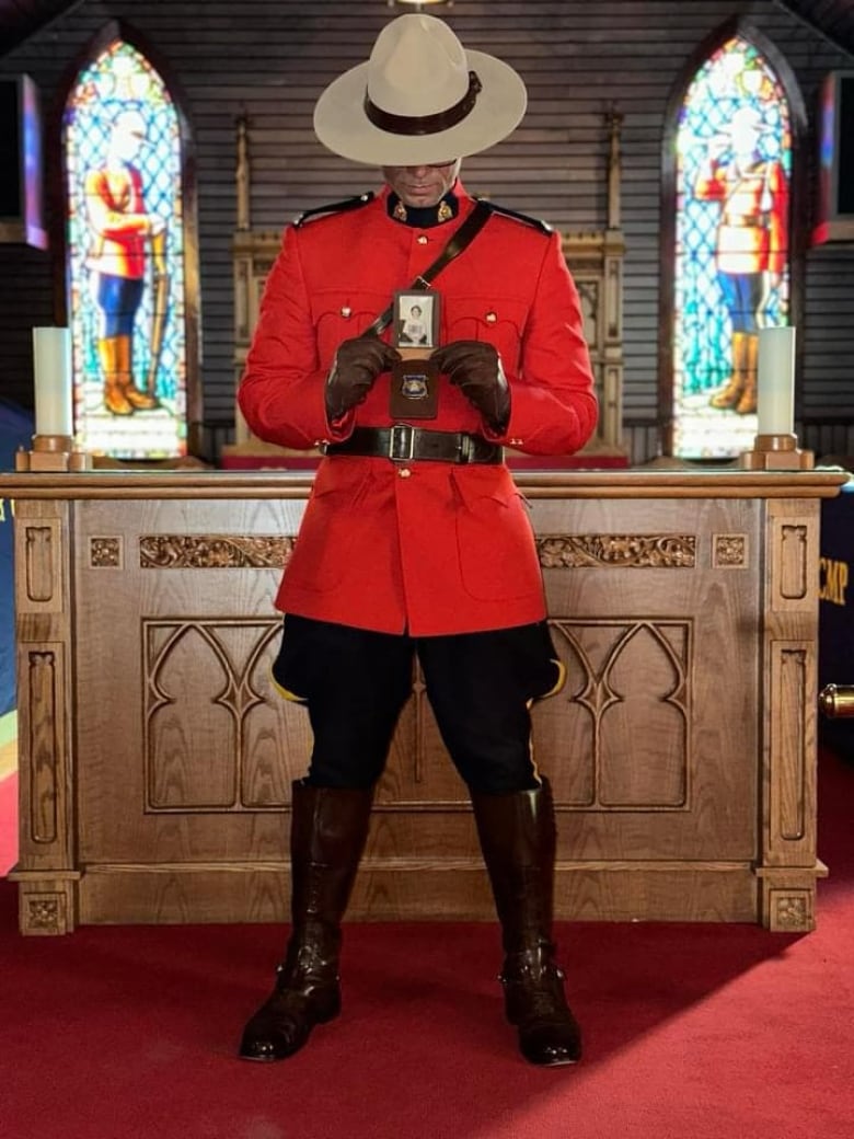 A man in RCMP Red Serge is standing in what appears to be a chapel. He is looking down at a photo he holds in his hands.