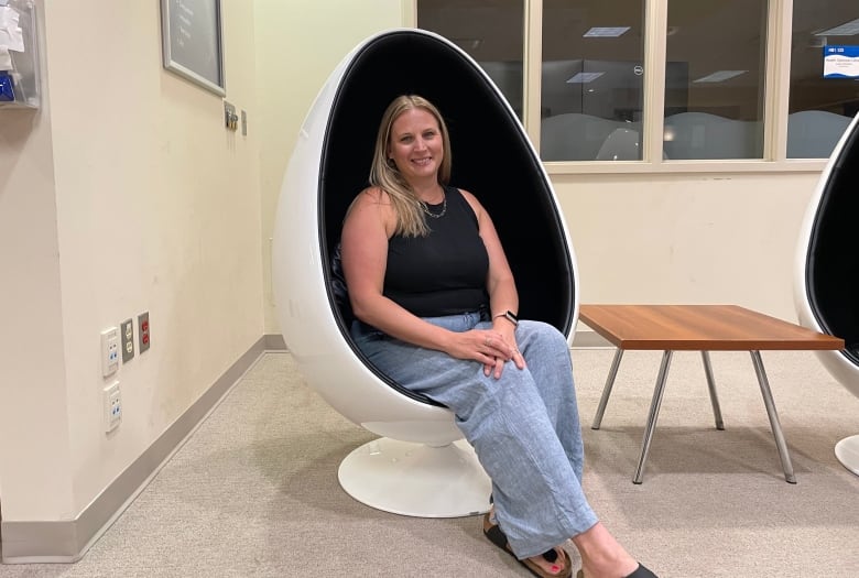 A smiling woman wearing jeans and a black tank top poses in an egg-shaped chair.