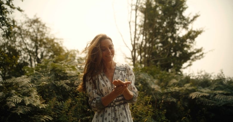 A person looking at something in their hand stands in front of trees.