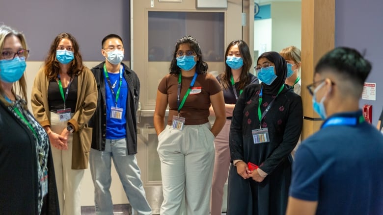 A group of students wearing surgical masks and lanyards stands around in a hospital setting.