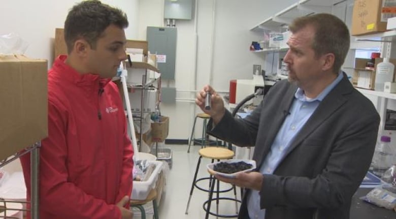 Darius Mahdavi talking with Johan Foster in a lab. Mahdavi is a man wearing a red jacket, and Foster is a man wearing a suit.