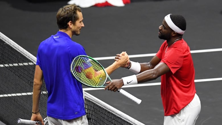 Two men's tennis players stand on opposite sides of the net and shake hands