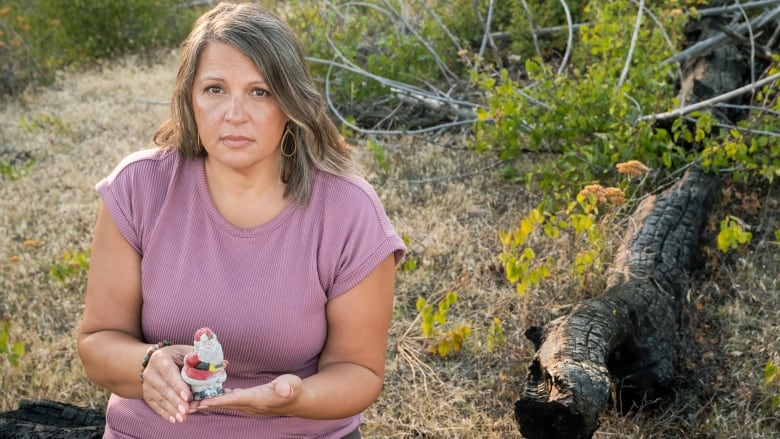 A white woman holds a scuffed Santa salt shaker as she sits on a burnt log.