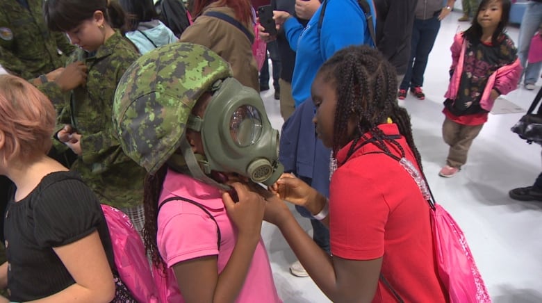 A young girl helps her friend buckle an oxygen mask worn by pilots during flight. 