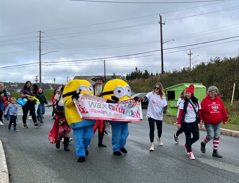 A group of people walks next to each other. Two people in Minions costumes hold a banner reading 