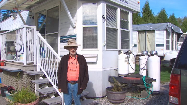 A man donning a hat in front of his mobile home in an RV park.