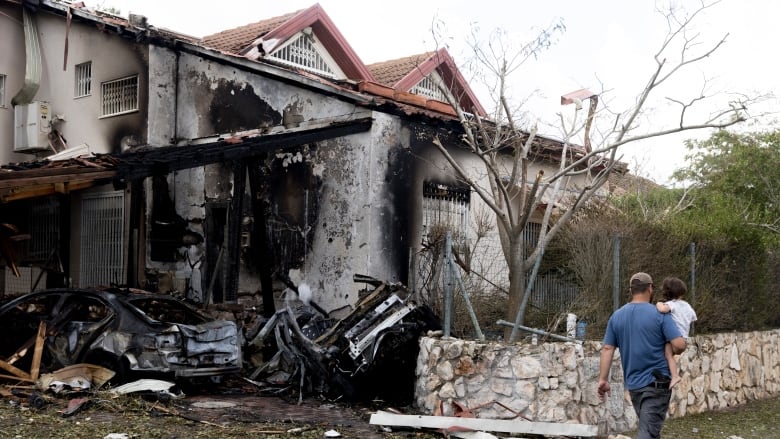 A man carries a baby at a scene of a heavily damaged and charred house.