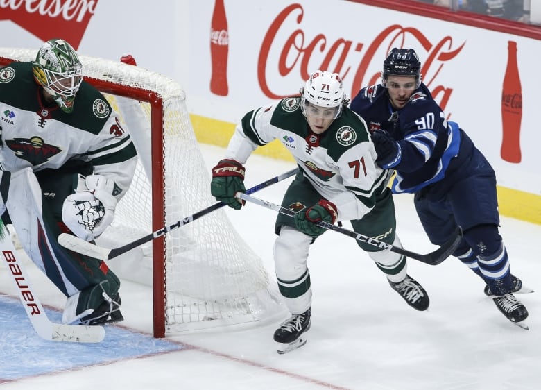 A hockey player in blue pushes against a player on the opposing team in a white and green uniform. 