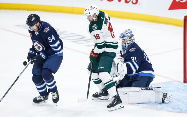 A hockey player in a blue and white uniform saves the puck near its team net. 