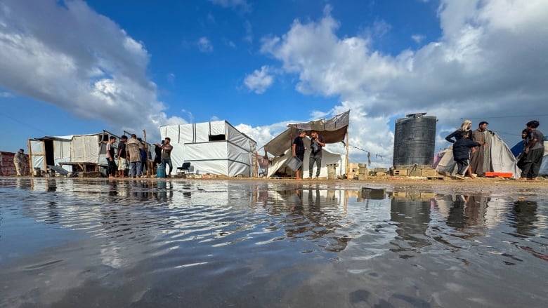 People stand outside a flooded tent camp.