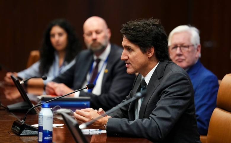 Trudeau sits at a conference table, wearing a grey suit and looking across the table and out of frame. 