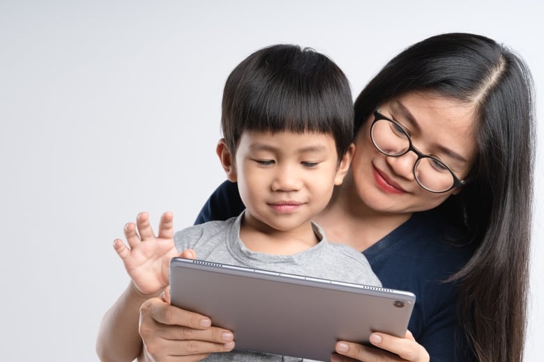 A mother is holding a boy child and they are looking at an iPad together. 