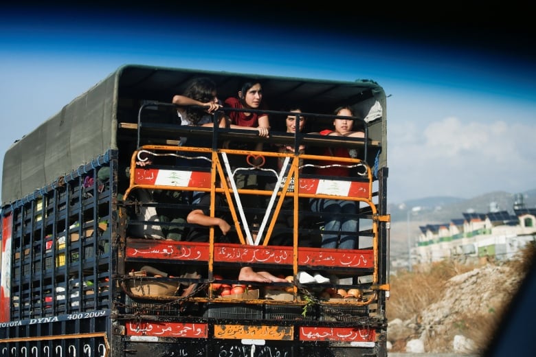 Children are seen riding in the back of a cargo truck as they evacuate town during an emergency.