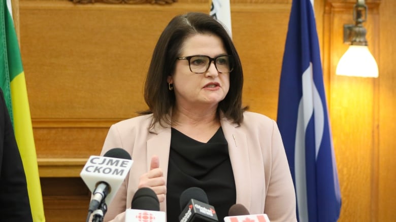 A woman stands with a podium in front of her. The woman is wearing a black shirt and pink blazer.