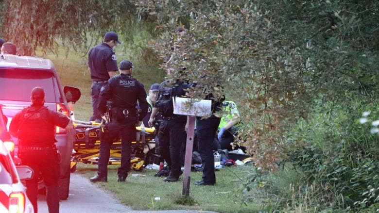 Police and emergency responders gather around a gurney in a grassy area.