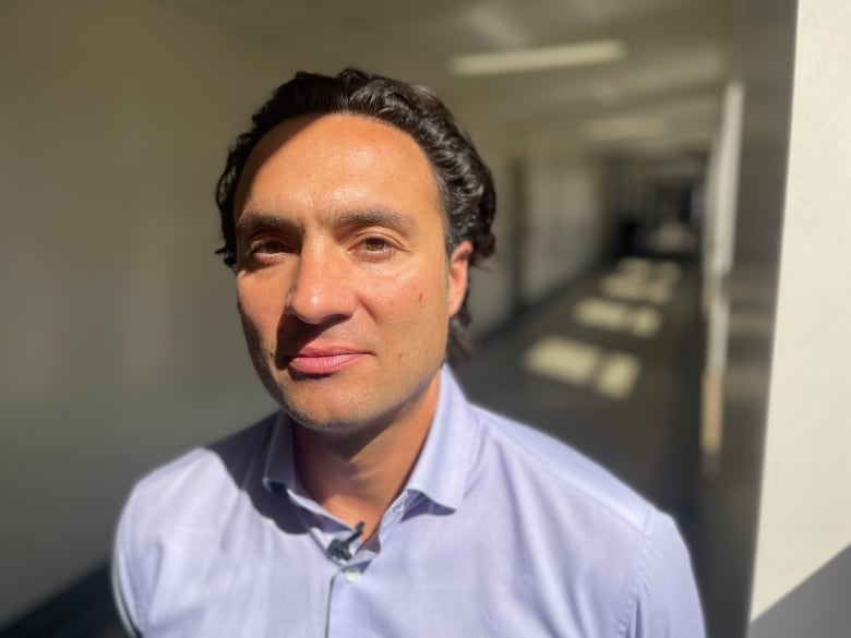 A man with a purple shirt smiles in a sunny hallway.