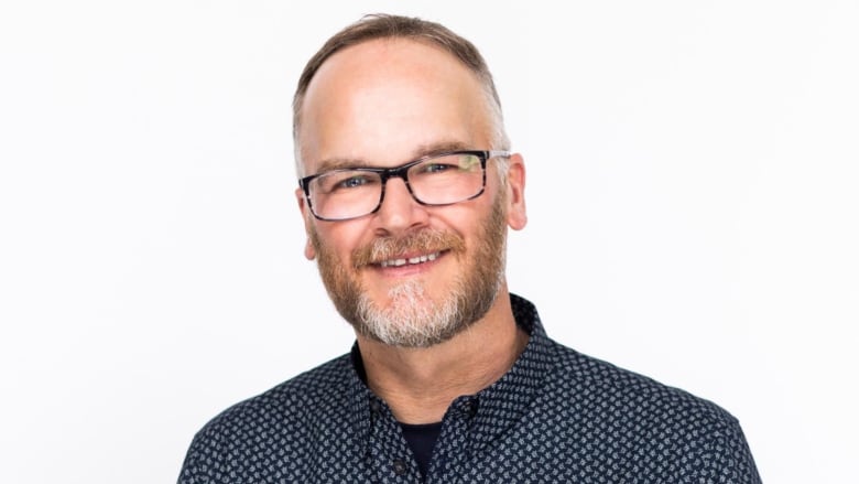 Portrait of a man with beard and glasses wearing a checkered button-up shirt.