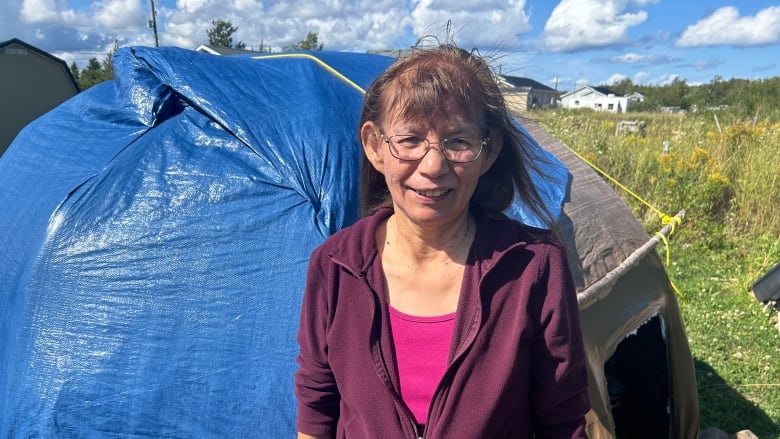 Woman standing outside structure covered with tarp.