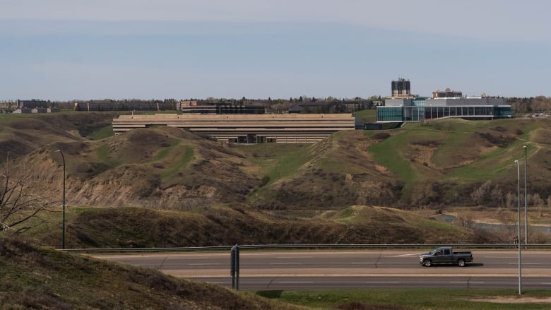 A vehicle drives on a road with green hills in the background