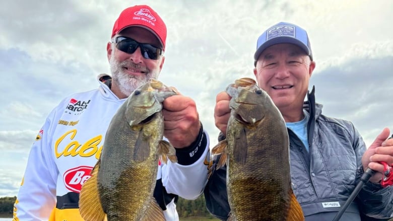 Two men stand in a boaty, each holding up a fish.