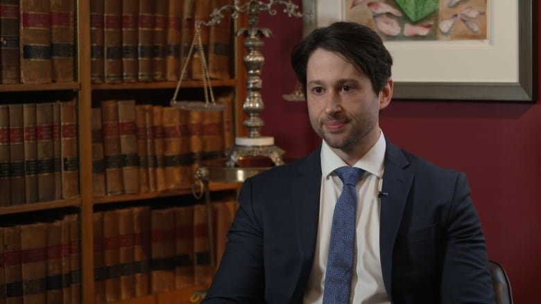 A man wearing a suit and tie looks to the left of the frame.