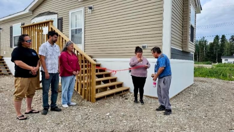 A man cuts a ribbon outside his new home while others watch