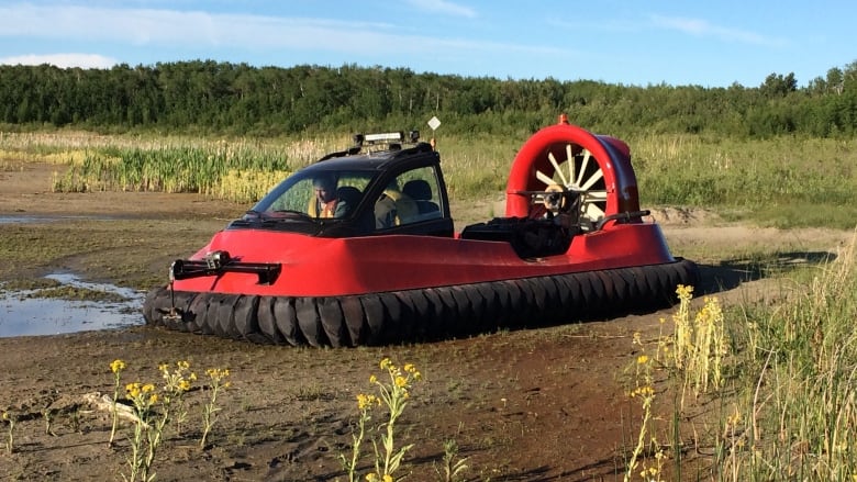 A red hovercraft at rest in a muddy clearing. 