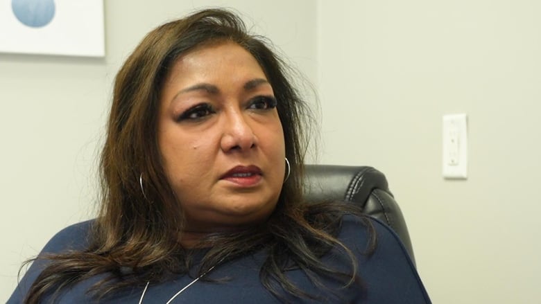 Middle-aged brown-skinned woman, pictured from the chest up. Brown hair. She is seated. 