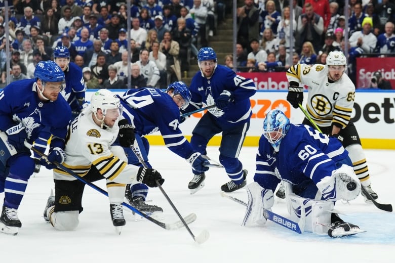 A male ice hockey goaltender makes a glove save from close range while down on both pads during a game in an arena filled with fans.