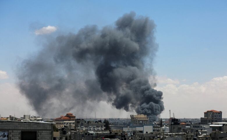 A large plume of smoke rises from a cityscape of low-lying buildings. 