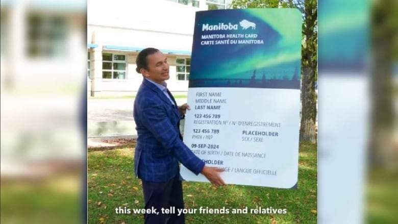 A man in a suit holds up an oversized version of a health card, with a northern lights design.