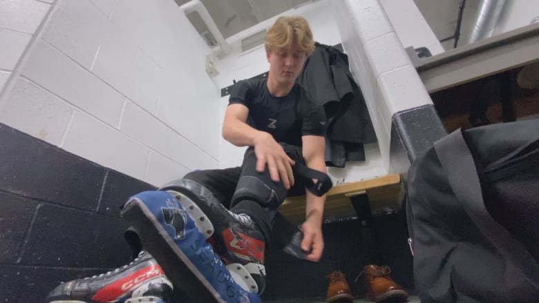 A man is seen from the floor of a locker room as he does up his skating equipment.