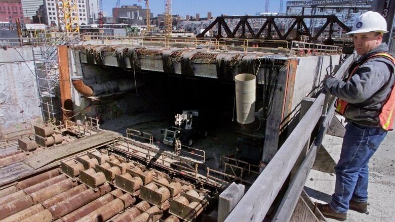 A construction worker looks at the camera. He is standing above an under-construction section of tunnel.