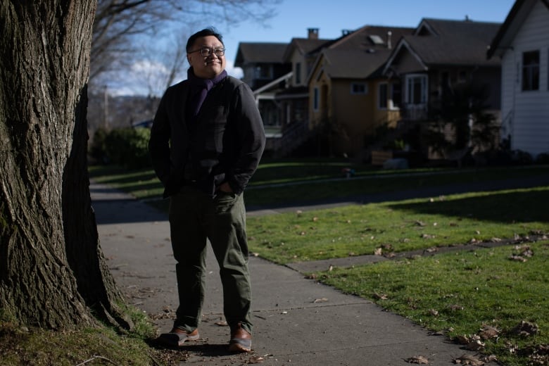 An East Asian man stands outdoors wearing a blazer on a sunny day.