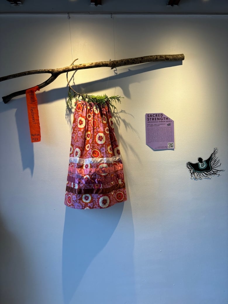 A ribbon skirt hangs on display at an art gallery.