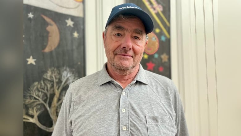 A man in a grey golf shirt and blue ball cap is shown.