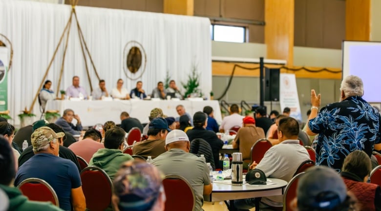 A large rooms of people, photographed from the back with one person at the microphone.