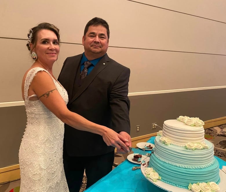 A couple, pose in a wedding dress in suit with a tie, while cutting their wedding cake.