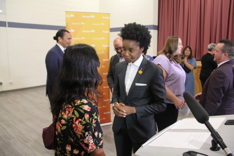 A person in a black suits talks to a person wearing a floral shirt. 