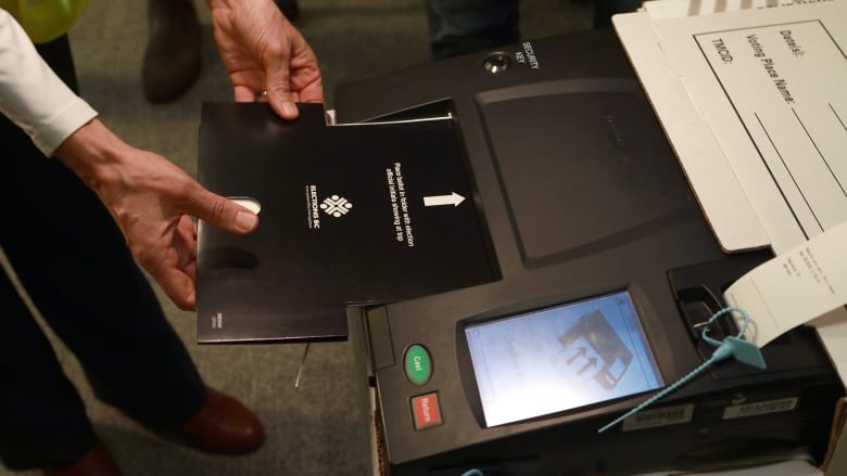 A person's hand is seen inserting a black voter card into a machine. 