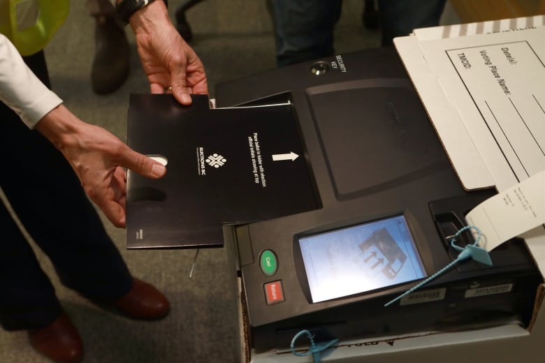 A person's hand is seen inserting a black voter card into a machine. 