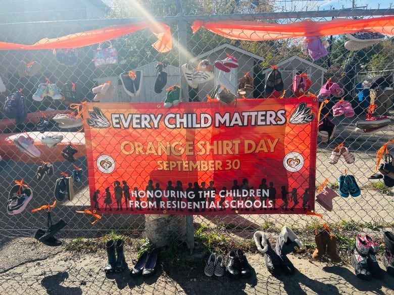 An orange sign ordains a wall of shoes on a sunny day. 